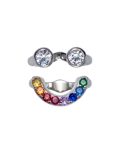 Silver ring with two large gemstones and a rainbow-colored band on a white background that forms a smiley face ring set