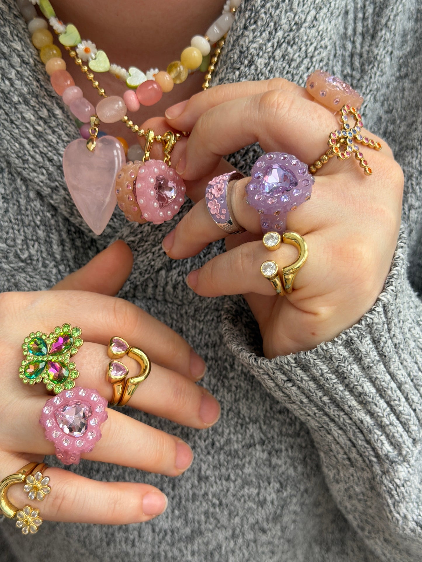 Close-up of hands wearing various colorful rings and a beaded necklace.