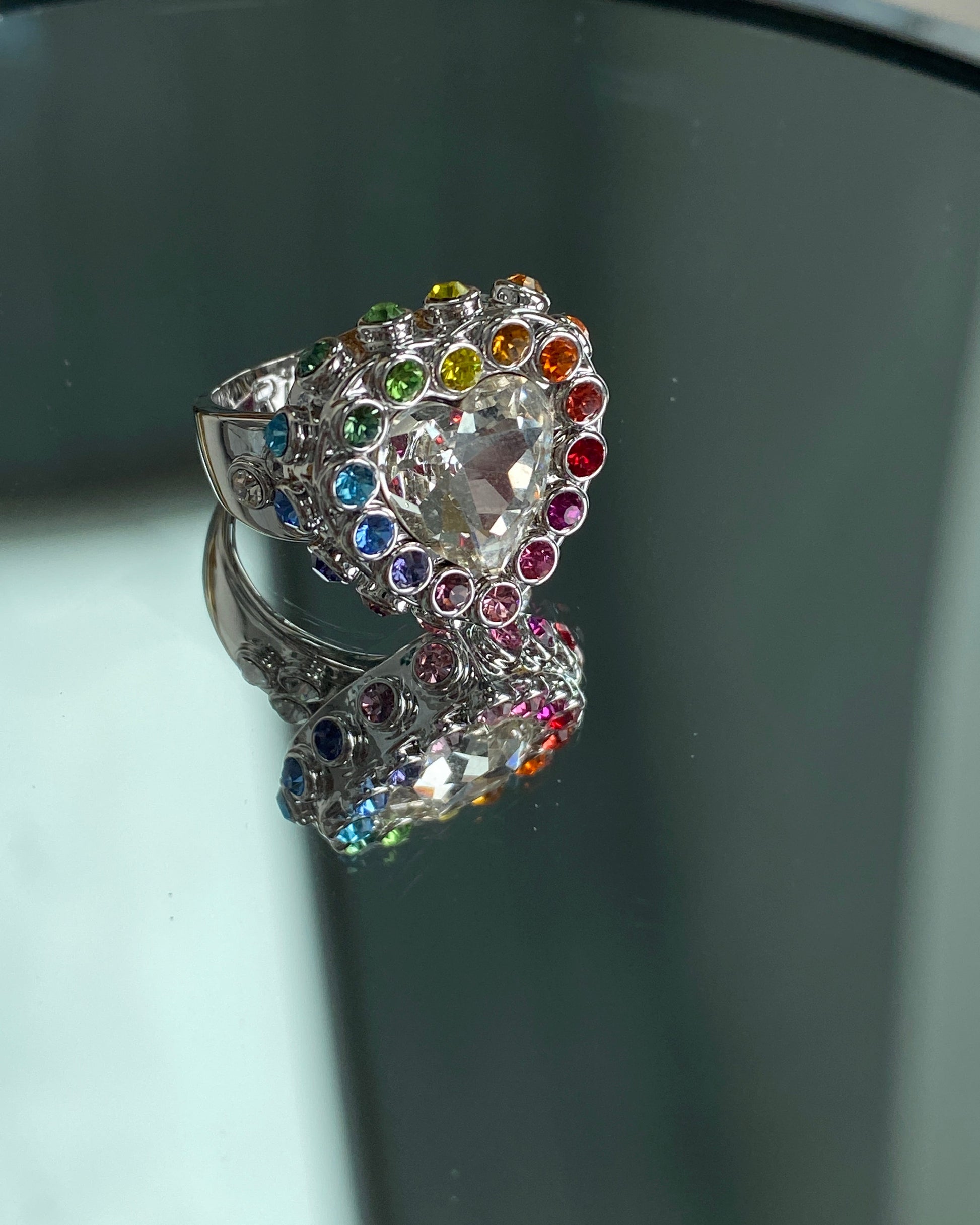 Heart-shaped ring with colorful gemstones on a reflective surface