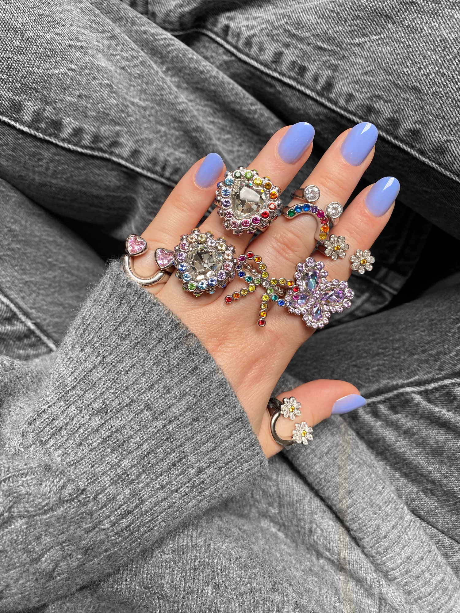 Hand wearing multiple colorful rings with a gray sweater and jeans background