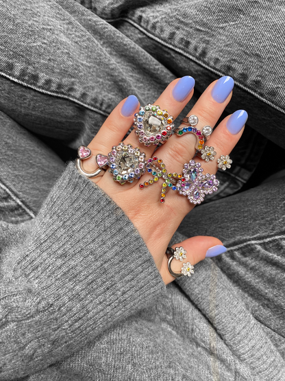 Hand wearing multiple colorful rings with a gray sweater and jeans background