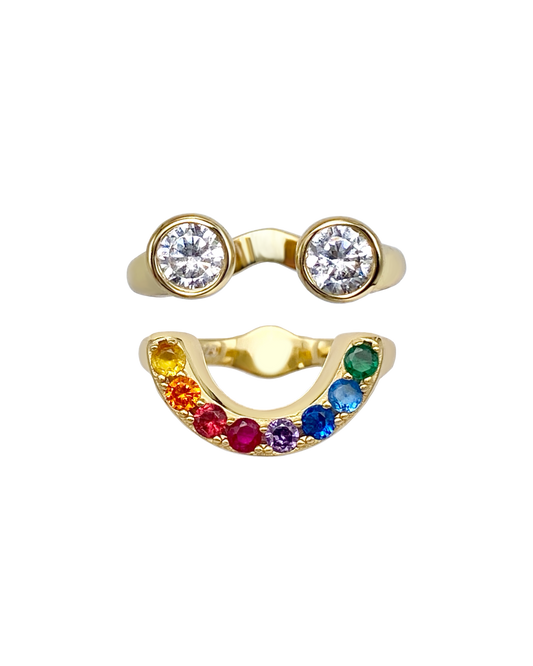 Gold ring with two circular gemstones and a rainbow-colored gemstone band that together form a smiley face ring set.
